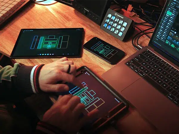 Hands playing DRUW on a tablet, with a phone, a second tablet and a laptop running DRUW on a studio desk